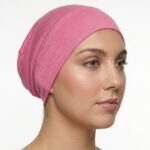 Side profile of a woman wearing a soft, stretchable cerise inner hijab cap against a white background