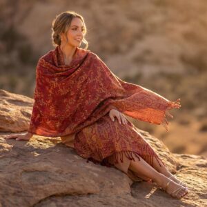 Rich crimson red pashmina shawl with vibrant golden amber jacquard floral patterns draped over a model during a warm desert sunset.