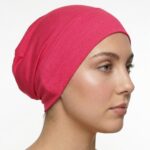 Side profile of a woman wearing a soft, stretchable hot-pink inner hijab cap against a white background