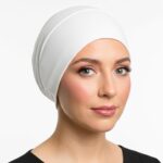 Side profile of a woman wearing a soft, stretchable off white inner hijab cap against a white background.