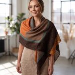 Model wearing a patchwork scarf in burnt orange and chocolate brown with teal chain link details.