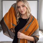 Model wearing a patchwork scarf in burnt orange and chocolate brown with teal chain link details.