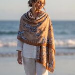 Woman at beach wearing a camel oversized scarf with blue equestrian horse-bit and chain motifs.