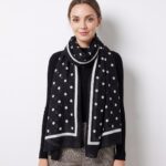 Model wearing a black scarf with white polka dots and a white border over a black sweater.